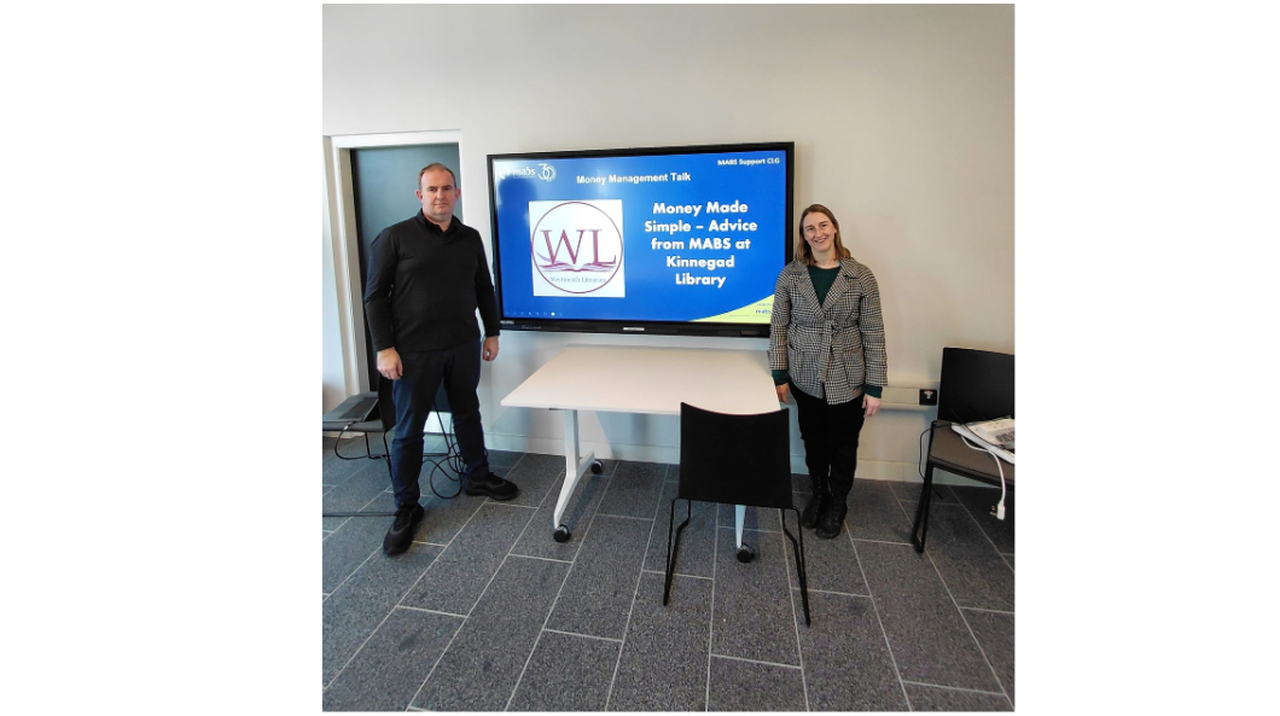 Two people stand next to a screen displaying 